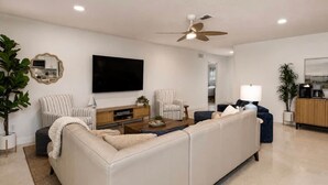A modern living room with a sectional sofa, a flat-screen TV, a ceiling fan, and a coffee machine. - Coastal Cactus- Pool+Pickleball+Putting Green+Shuffleboard! (Manatee County)