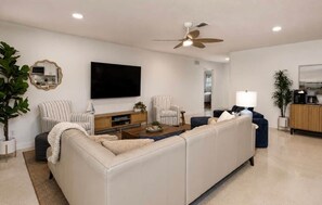 A modern living room with a sectional sofa, a flat-screen TV, a ceiling fan, and a coffee machine. - Coastal Cactus- Pool+Pickleball+Putting Green+Shuffleboard! (Manatee County)