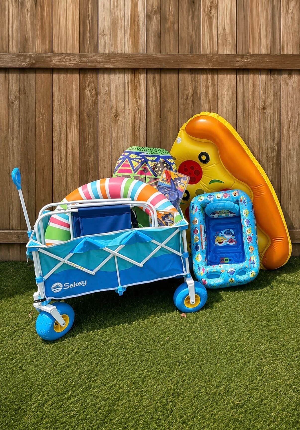A blue and white baby stroller with a canopy, a colorful beach ball, and an inflatable dinosaur toy against a wooden fence backdrop.