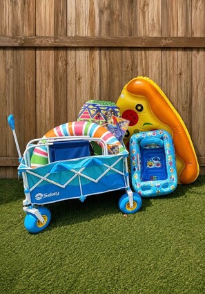 A blue and white baby stroller with a canopy, a colorful beach ball, and an inflatable dinosaur toy against a wooden fence backdrop. - Coastal Cactus- Pool+Pickleball+Putting Green+Shuffleboard! (Manatee County)