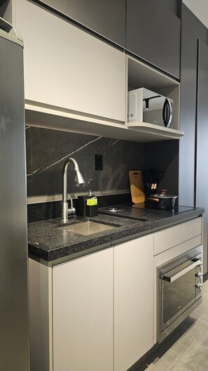 Una cocina moderna con microondas integrado, pileta de acero inoxidable y horno.
