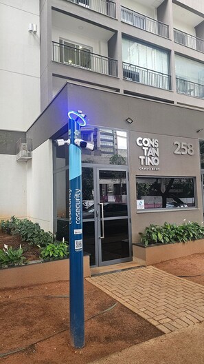 Un poste de sécurité avec un code QR et une pancarte indiquant « CONS TANO 258 CANPO BELO » devant un immeuble doté d’un balcon.