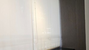 Ein Zimmer mit einem großen Fenster, einer dunklen Bank und einem teilweisen Blick auf ein Bett.