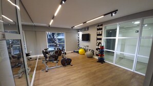 Ein Fitnessraum mit Trainingsgeräten, einem an der Wand befestigten Fernseher und einem großen Fenster.