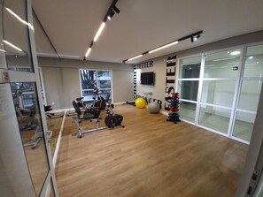 Ein Fitnessraum mit Trainingsgeräten, einem an der Wand befestigten Fernseher und einem großen Fenster.