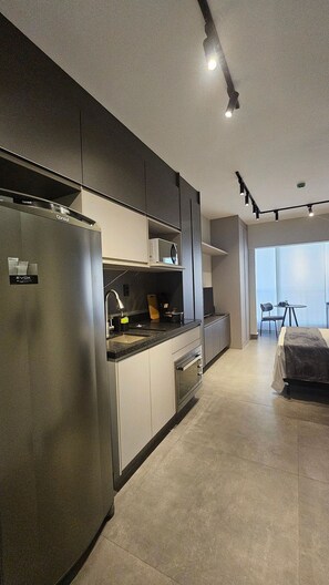 A modern kitchen with a built-in refrigerator, oven, and microwave. There is a dining area with a table and chairs visible in the background. - Cond. Constantino Campo Belo NR (São Paulo)
