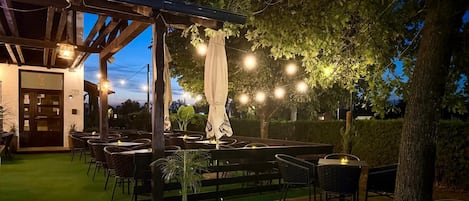 An outdoor patio area with tables and chairs, string lights, and a pergola structure.