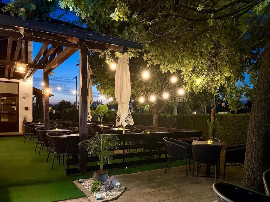 Een terras buiten met tafels, stoelen, lichtslingers en een pergola.