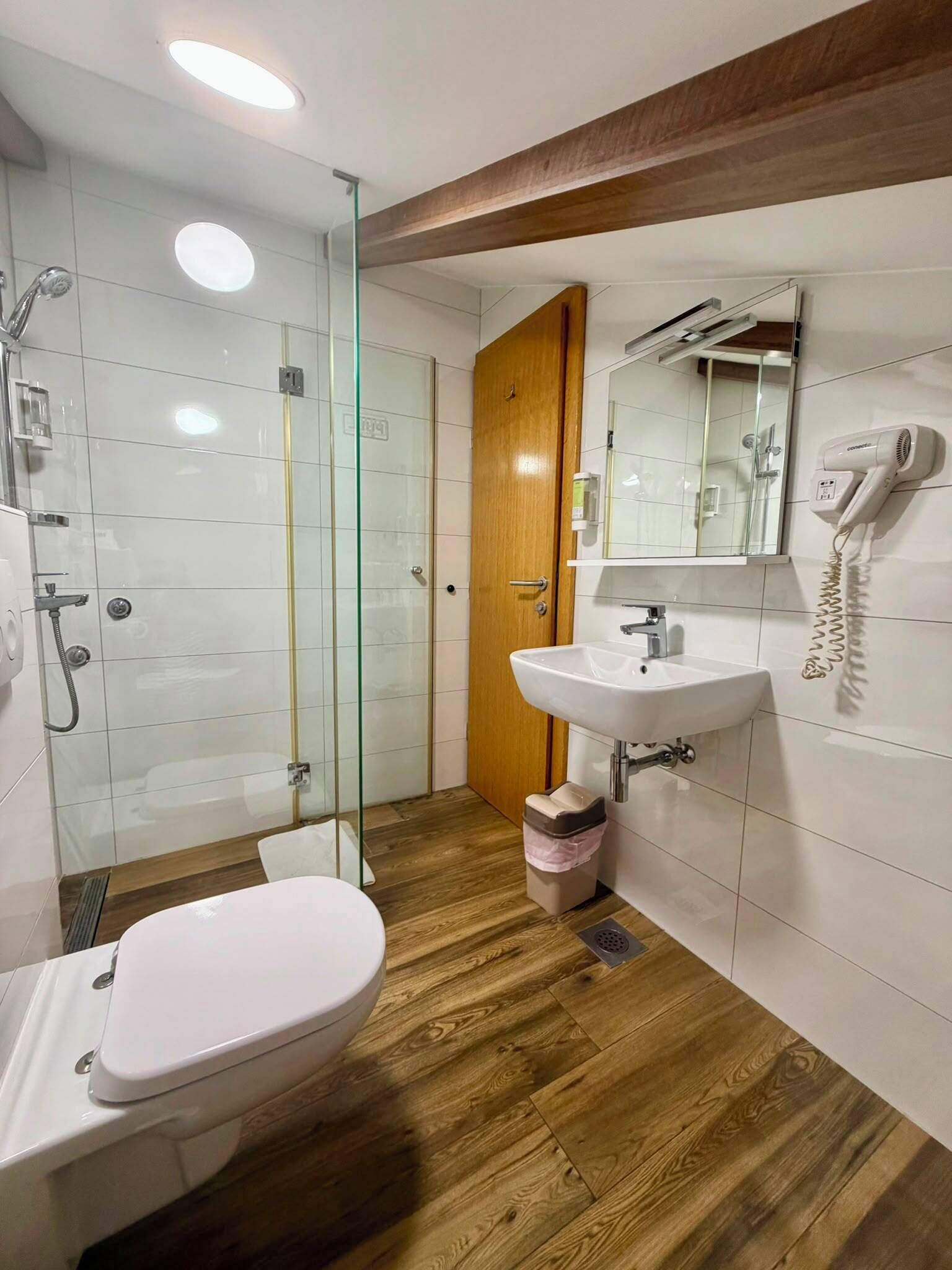Un baño moderno con cabina de ducha de vidrio, puerta de madera, lavabo blanco y retrete.