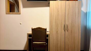 A hotel room with two beds, a TV mounted on the wall, a wooden wardrobe, a chair, and a guitar.
