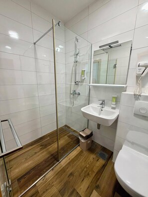Un baño moderno con cabina de ducha de vidrio, un lavamanos blanco y un espejo encima.