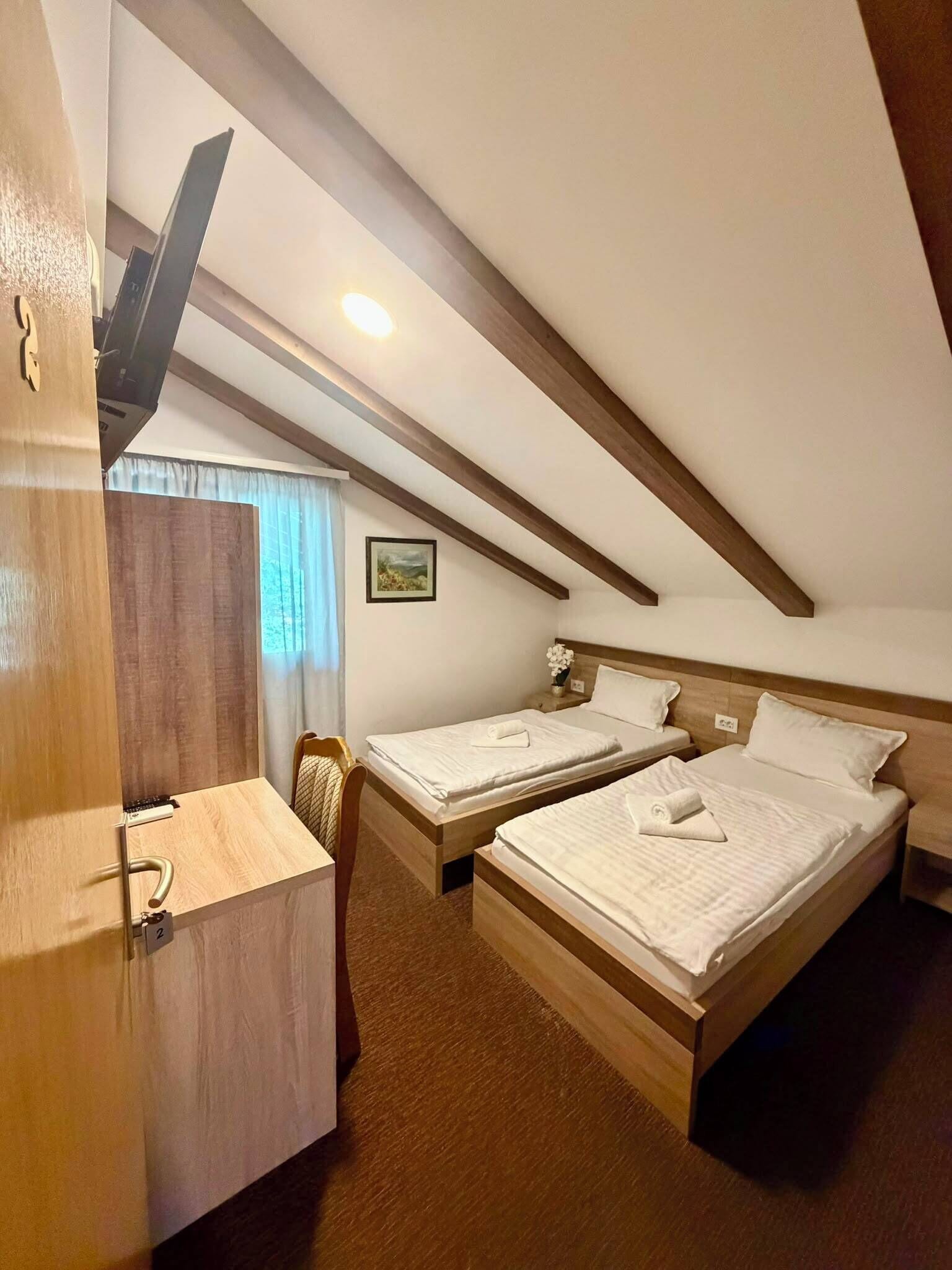 A room with two wooden beds, a desk, and a ceiling fan.