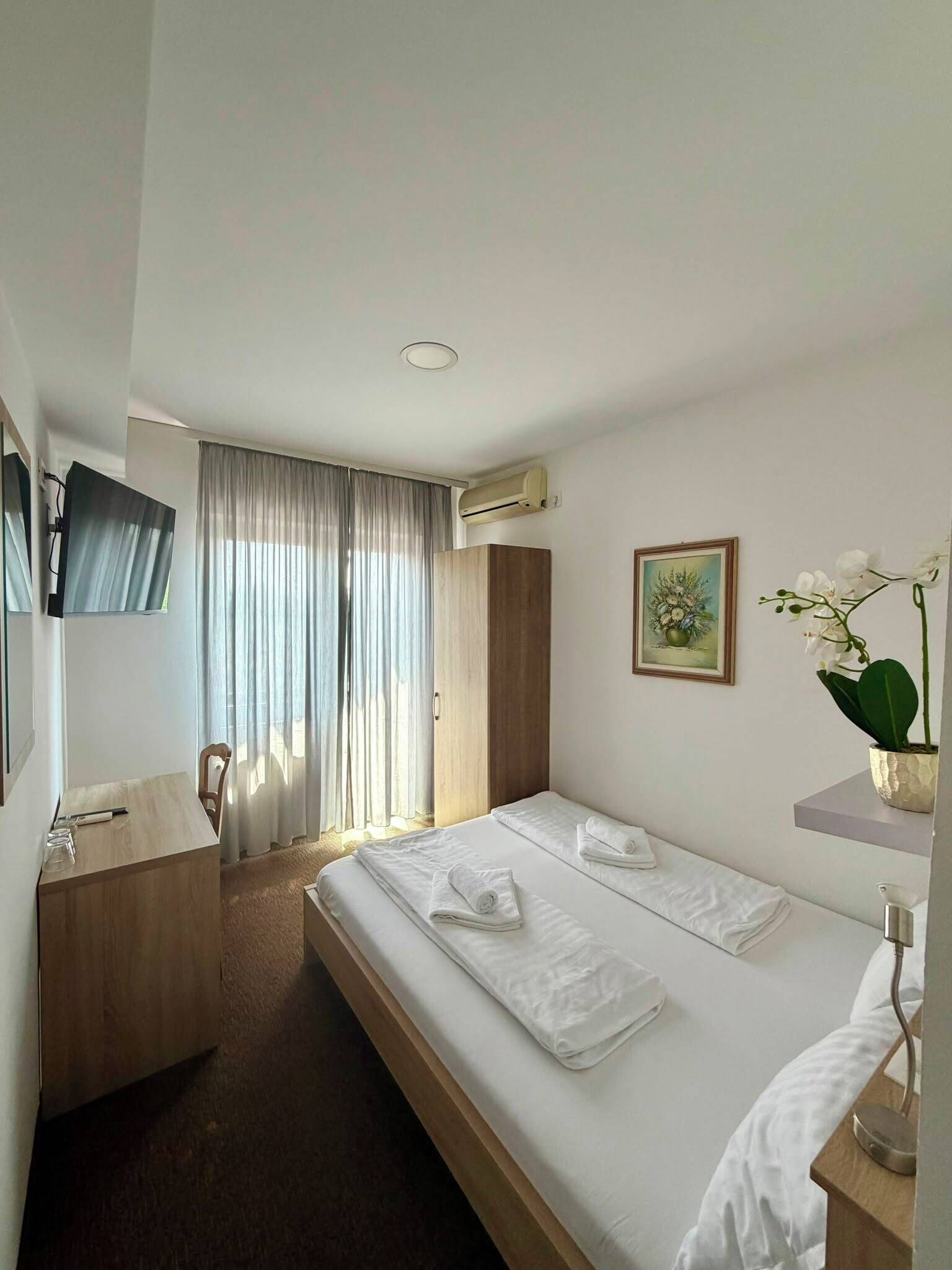 Una habitación de hotel con cama, escritorio, silla, televisión y ventana con cortinas.