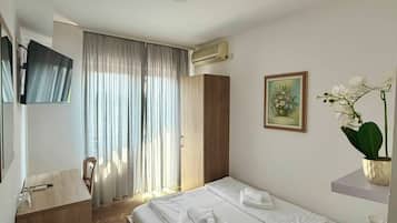 Una habitación de hotel con cama, escritorio, silla, televisión y ventana con cortinas.