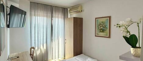 A hotel room with a bed, a desk, a chair, a TV, and a window with curtains.