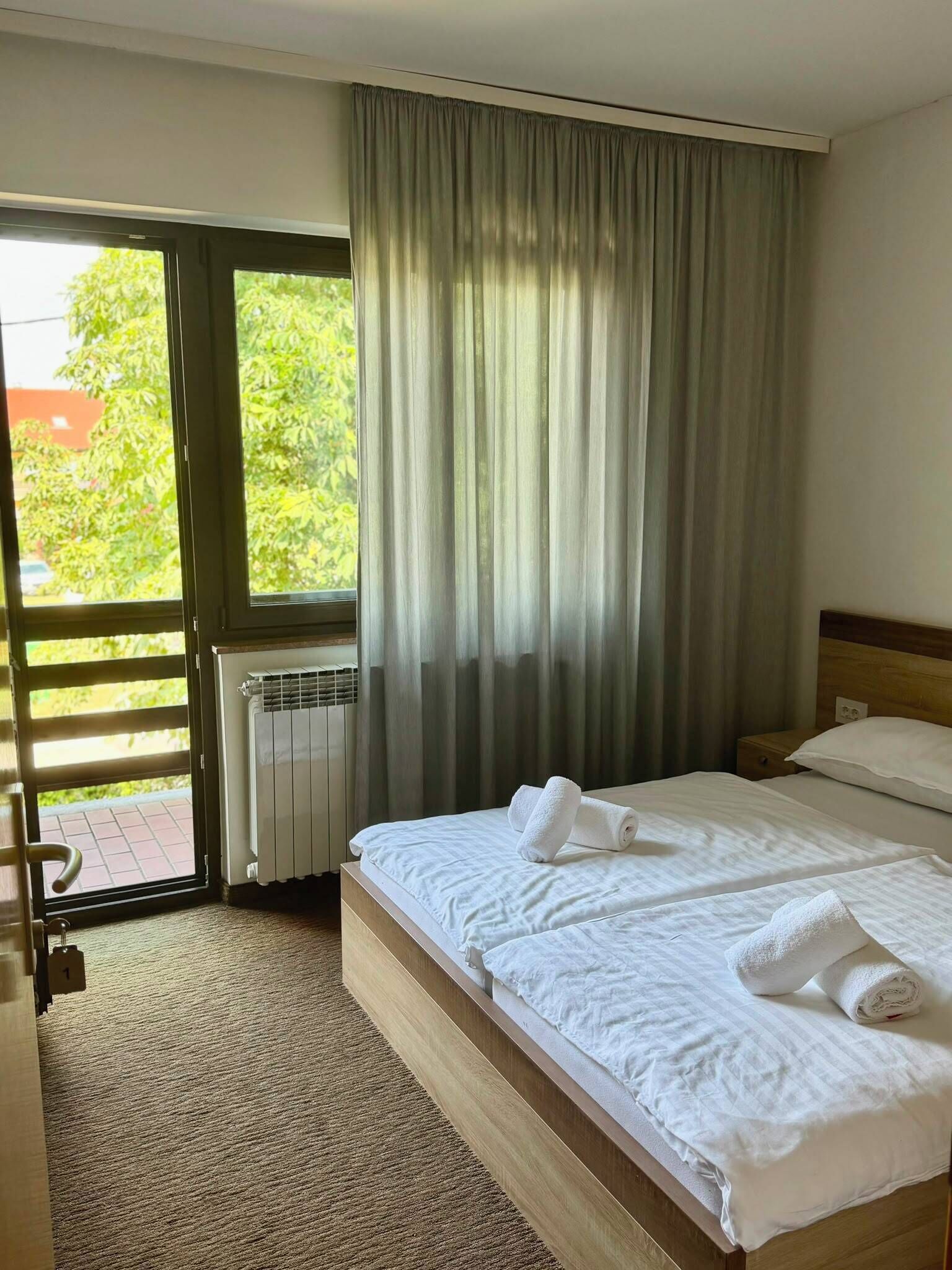 Una habitación de hotel con cama, un radiador, una ventana con cortinas y vistas a zonas verdes.