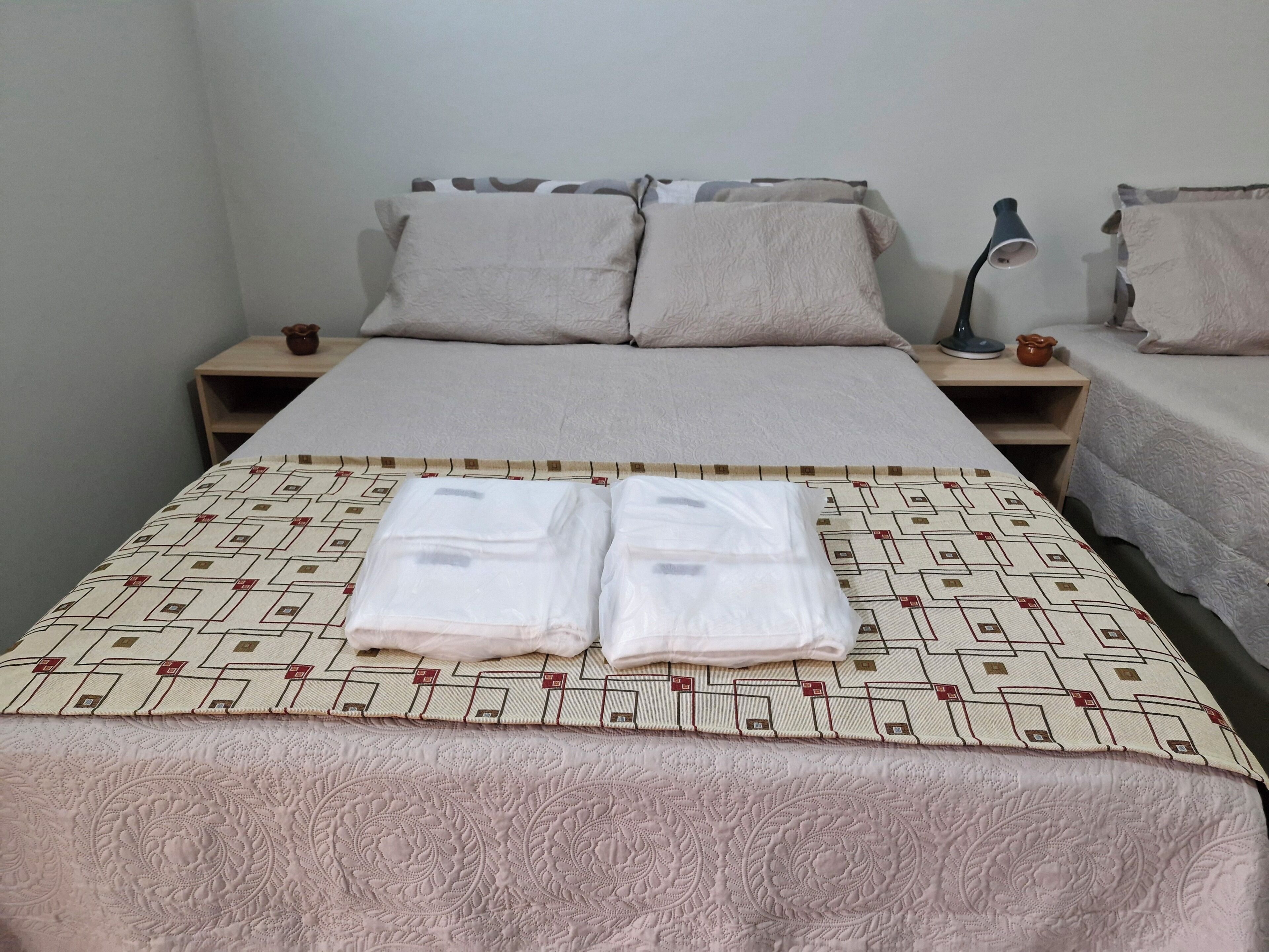 A neatly made bed with a patterned bedspread and two pillows, a bedside lamp, and a small decorative item on the nightstand.