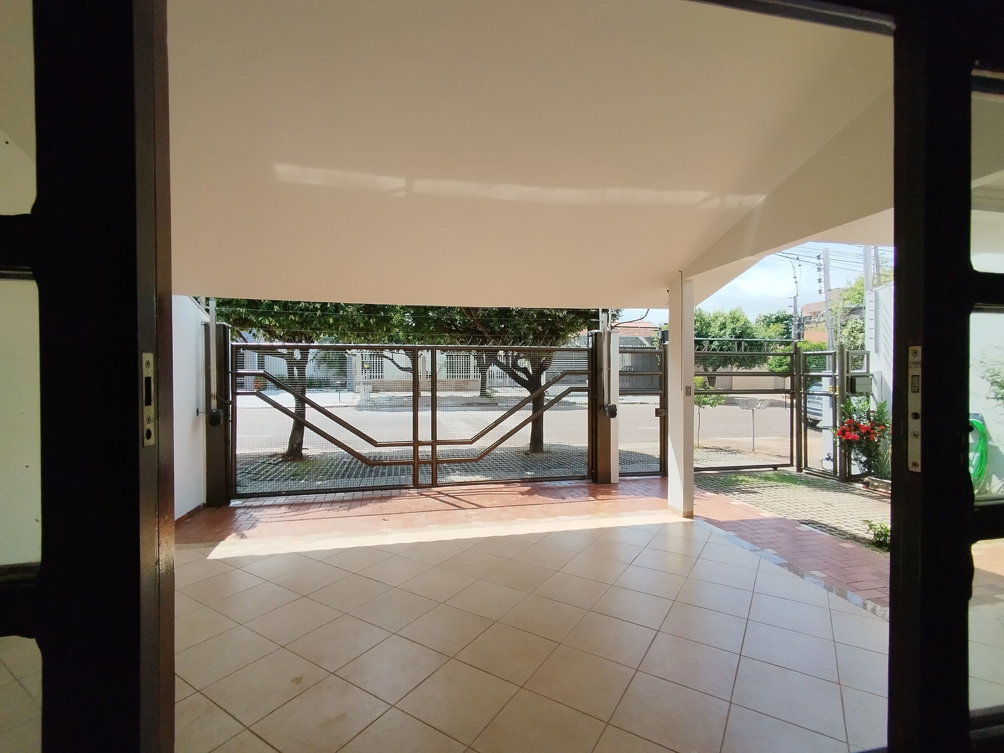 Une entrée ouverte donnant sur un bâtiment dont le sol est recouvert de carreaux et qui est protégée par une grille métallique menant à l’extérieur.