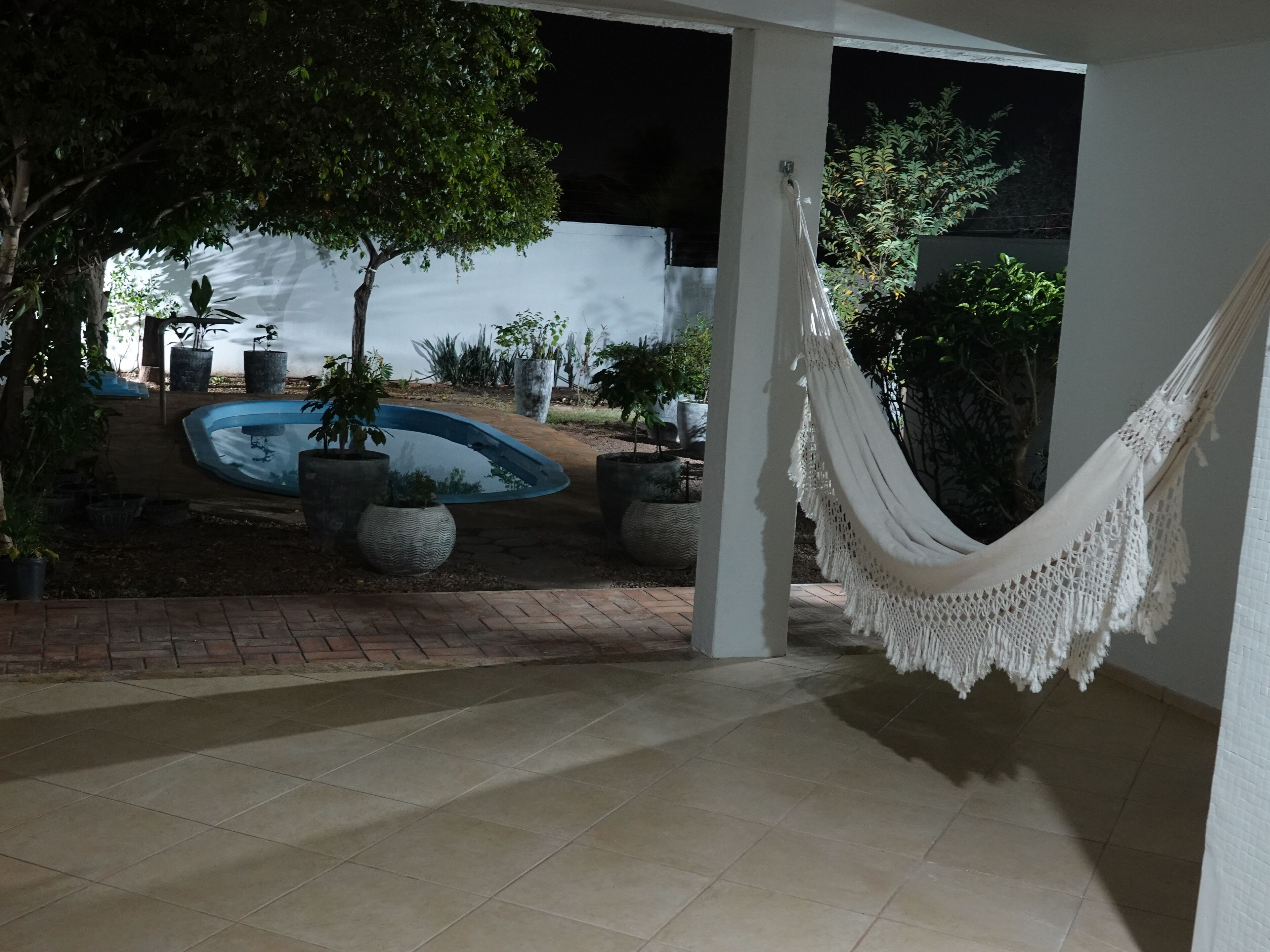 A tiled patio area with a hammock, potted plants, and a swimming pool.