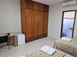 A room with a wooden wardrobe, a small refrigerator, a desk with a chair, and two beds with towels. - Pousada Solar dos Passaros (Rondonópolis)