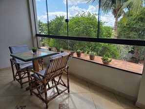 A balcony with a glass table and chairs, potted plants, and a view of greenery.