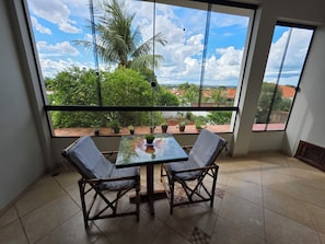 Varanda com mesa de vidro e duas cadeiras, vista para um jardim e edifícios.