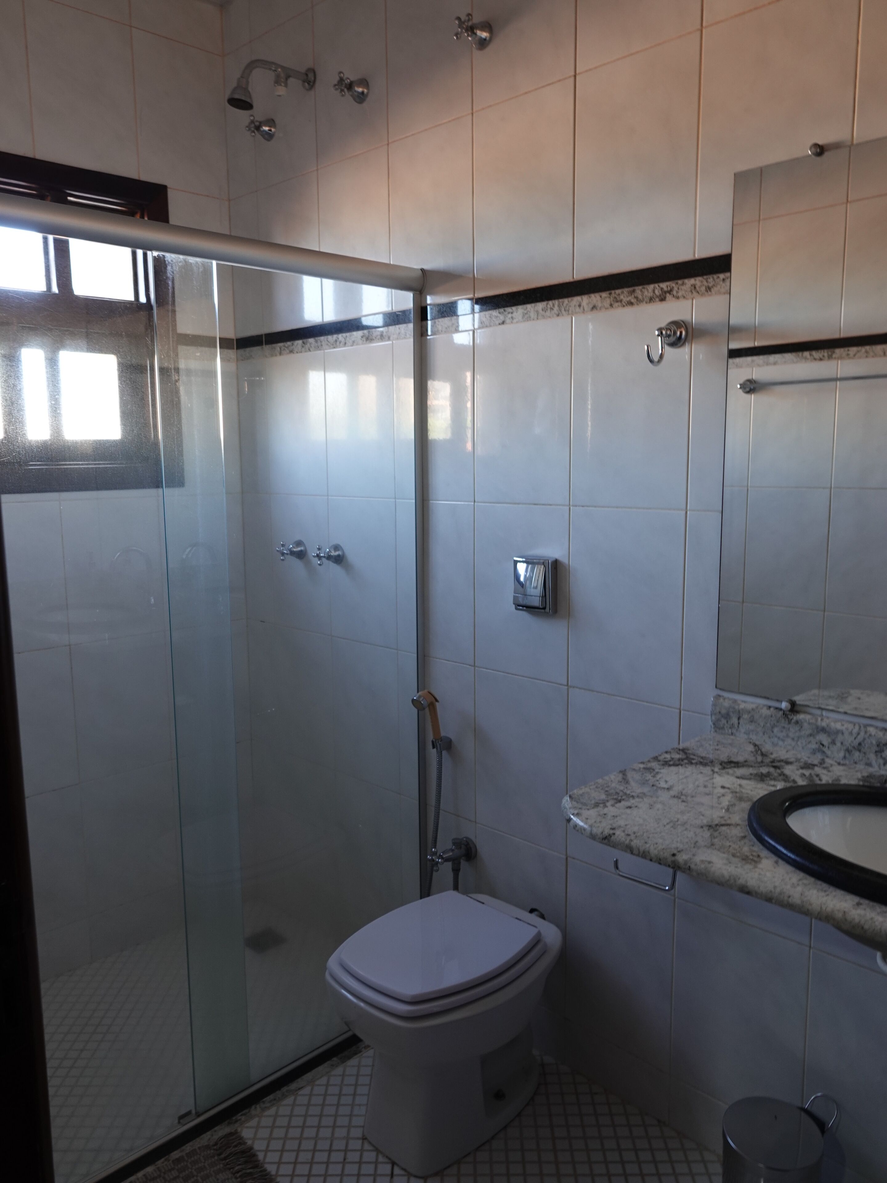 A bathroom with a glass-enclosed shower, a toilet, and a sink with a marble countertop.