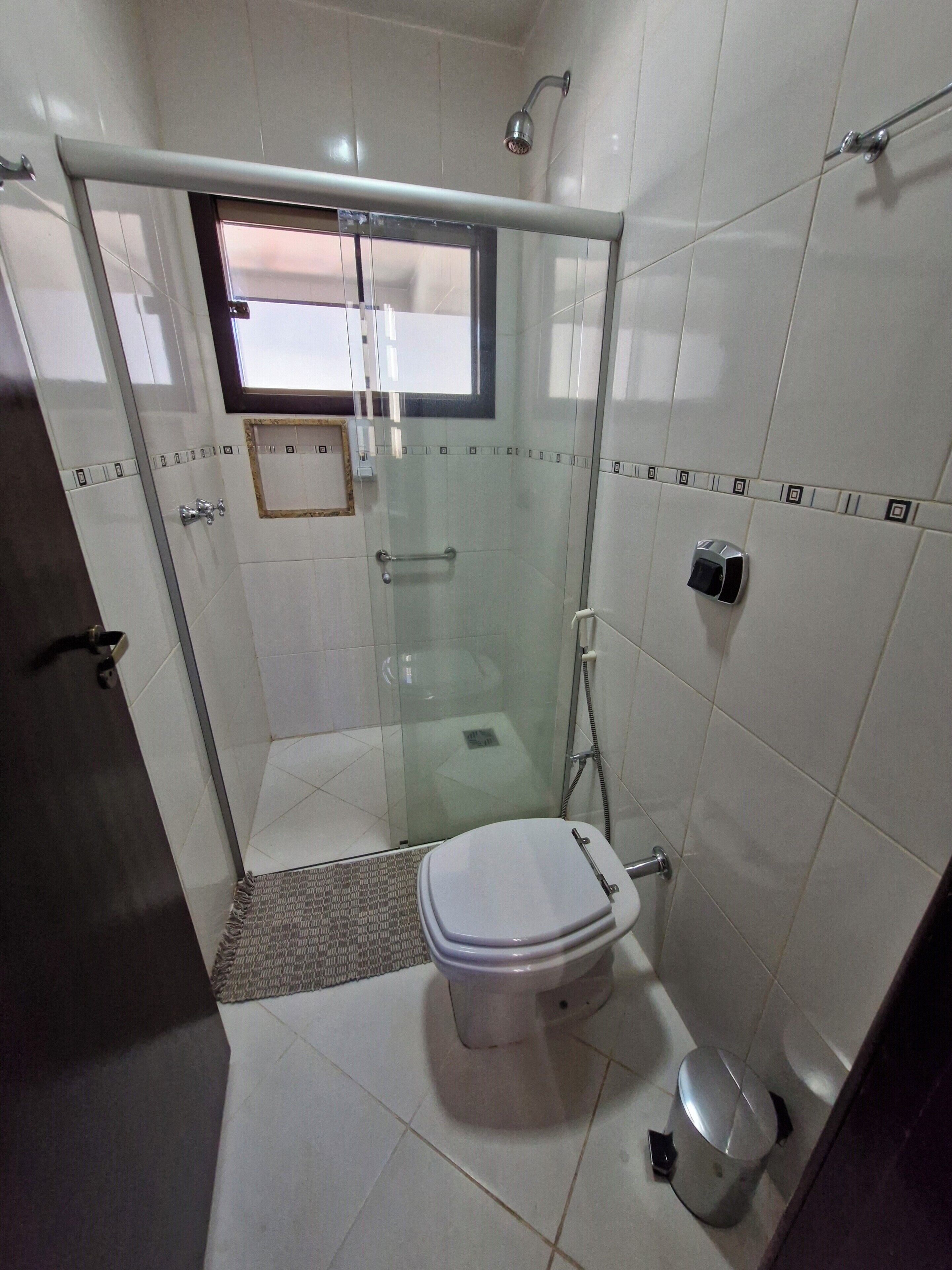 A small bathroom with a toilet, a glass-enclosed shower, and a window.