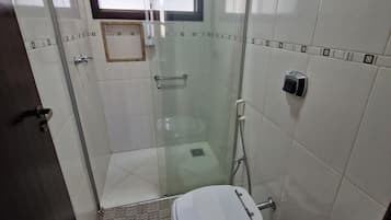 A small bathroom with a toilet, a glass-enclosed shower, and a window.