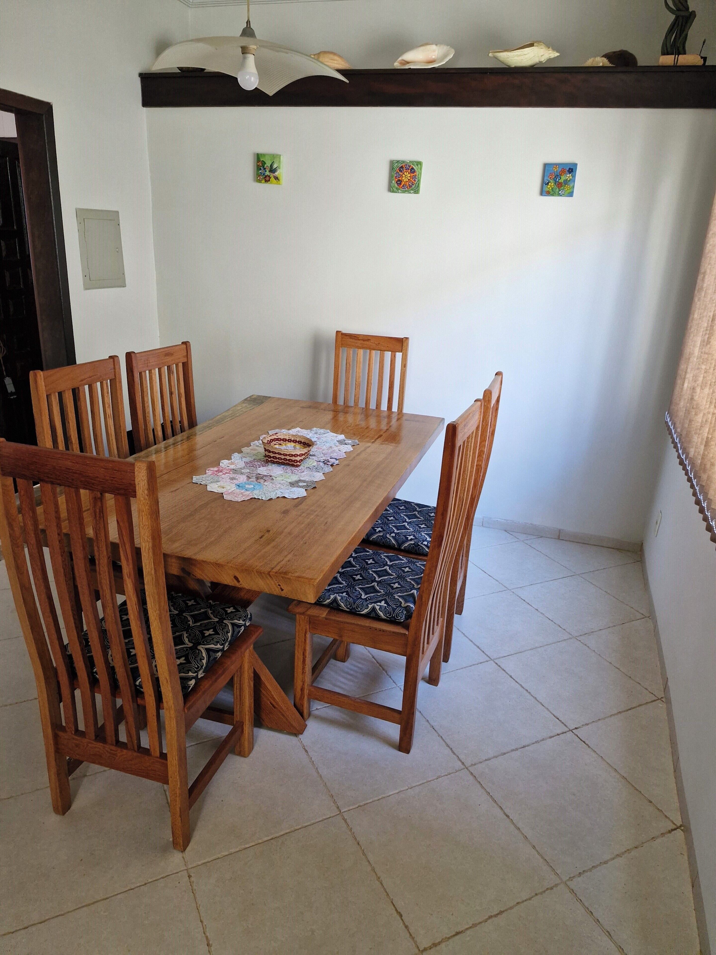 Uma mesa de jantar de madeira com quatro cadeiras, toalha de renda e um objeto decorativo.
