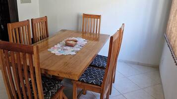 Uma mesa de jantar de madeira com quatro cadeiras, toalha de renda e um objeto decorativo.