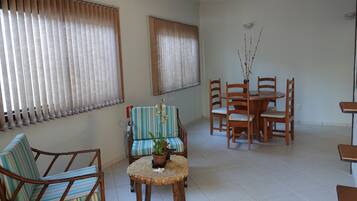 A room with a dining table, chairs, a sofa, and a small round table with a plant.