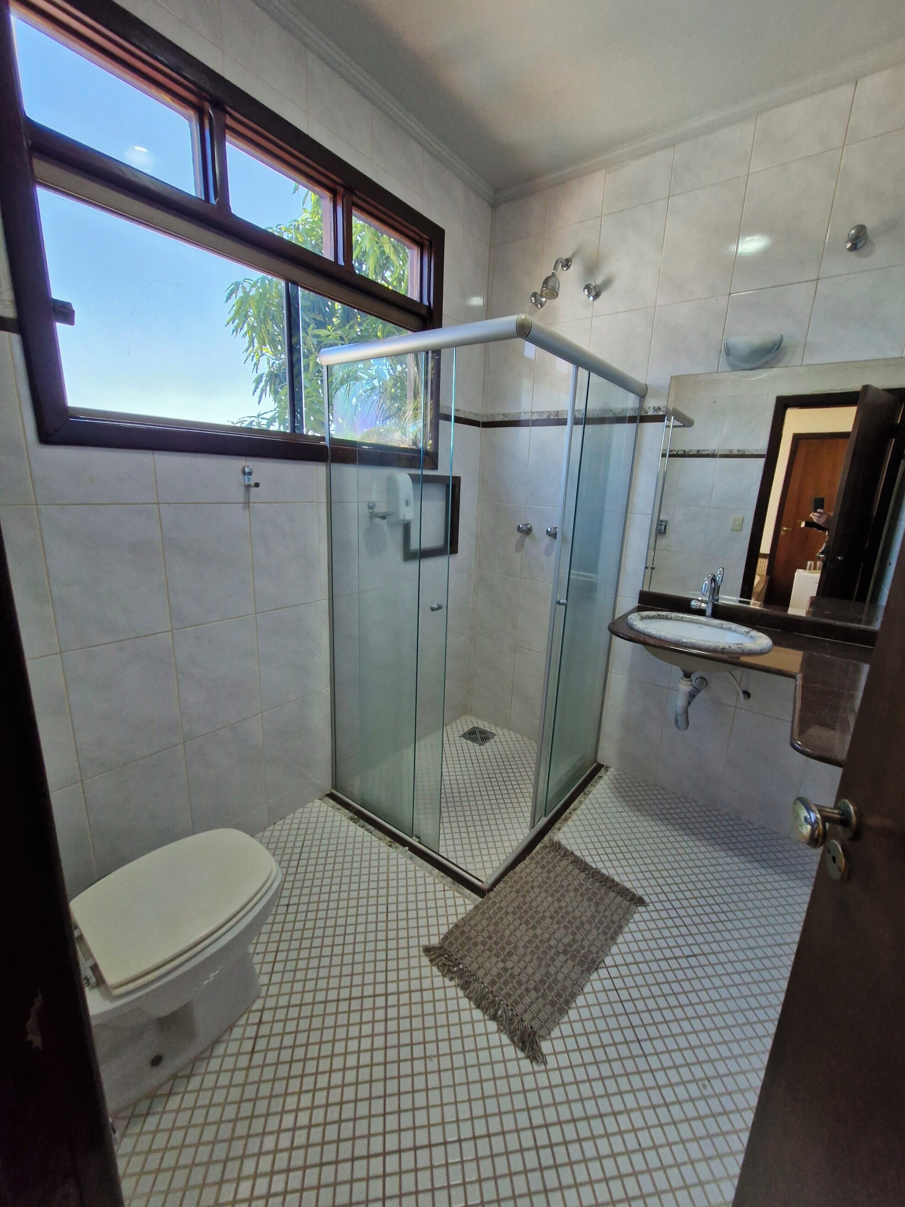 A bathroom with a glass-enclosed shower, a toilet, a sink with a mirror, and a window providing natural light.