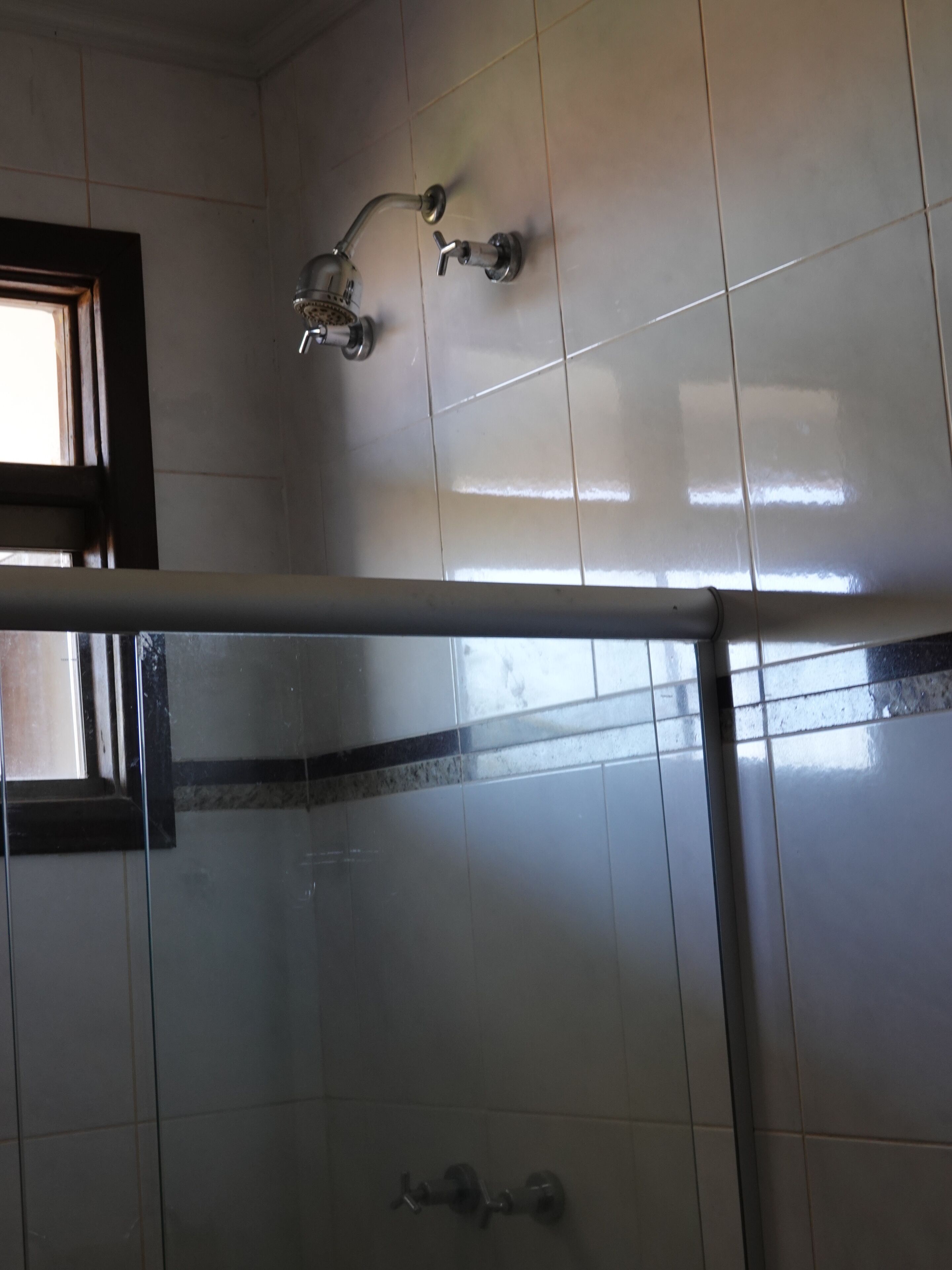 Une salle de bain avec des murs carrelés de carreaux blancs, un espace douche et une fenêtre.