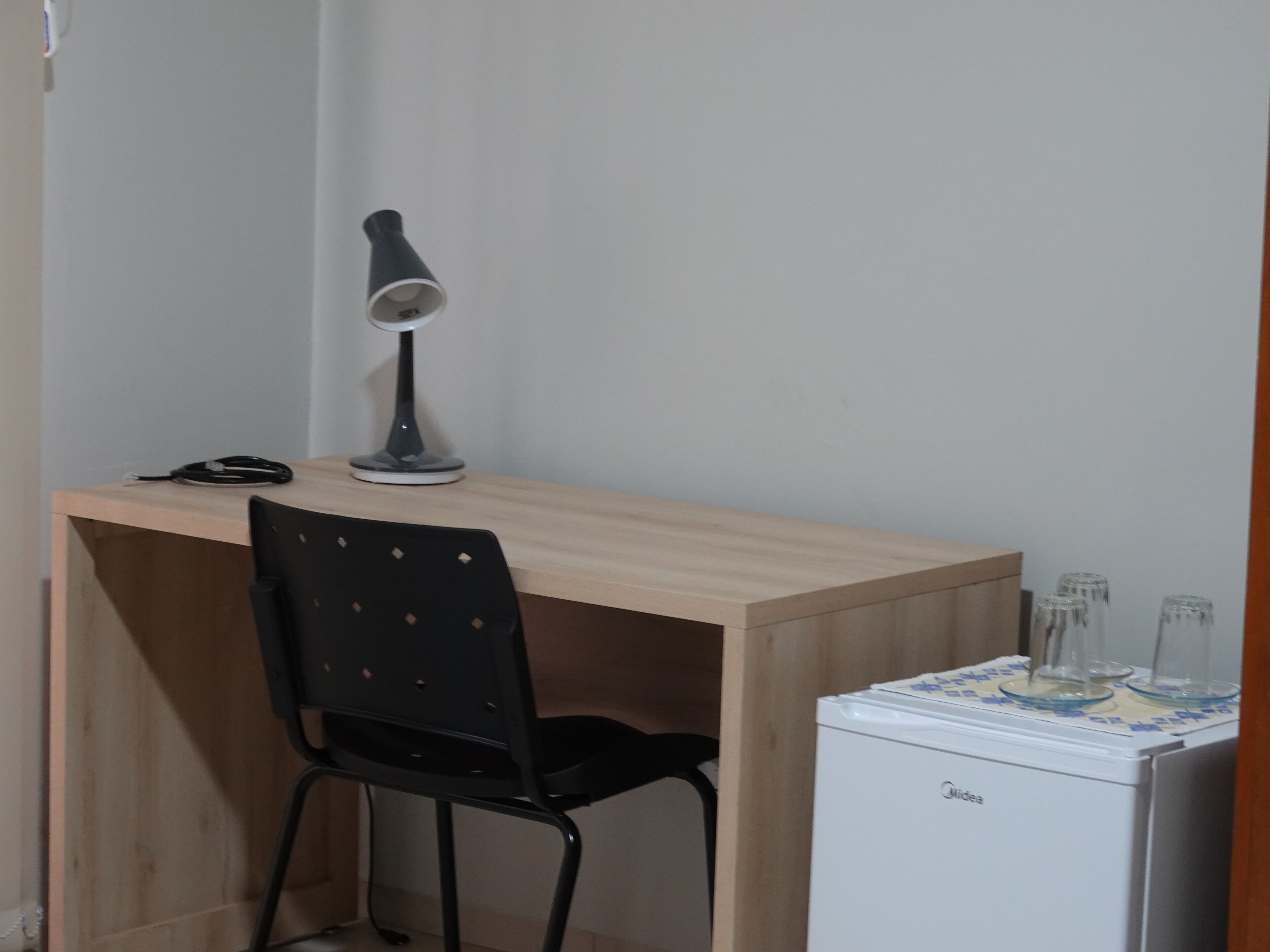 A small workspace with a desk, a chair, a lamp, and a compact refrigerator.