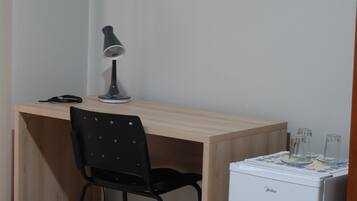 A small workspace with a desk, a chair, a lamp, and a compact refrigerator.