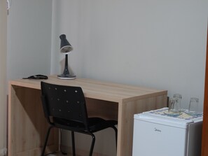 A small workspace with a desk, a chair, a lamp, and a compact refrigerator. - Pousada Solar dos Passaros (Rondonópolis)