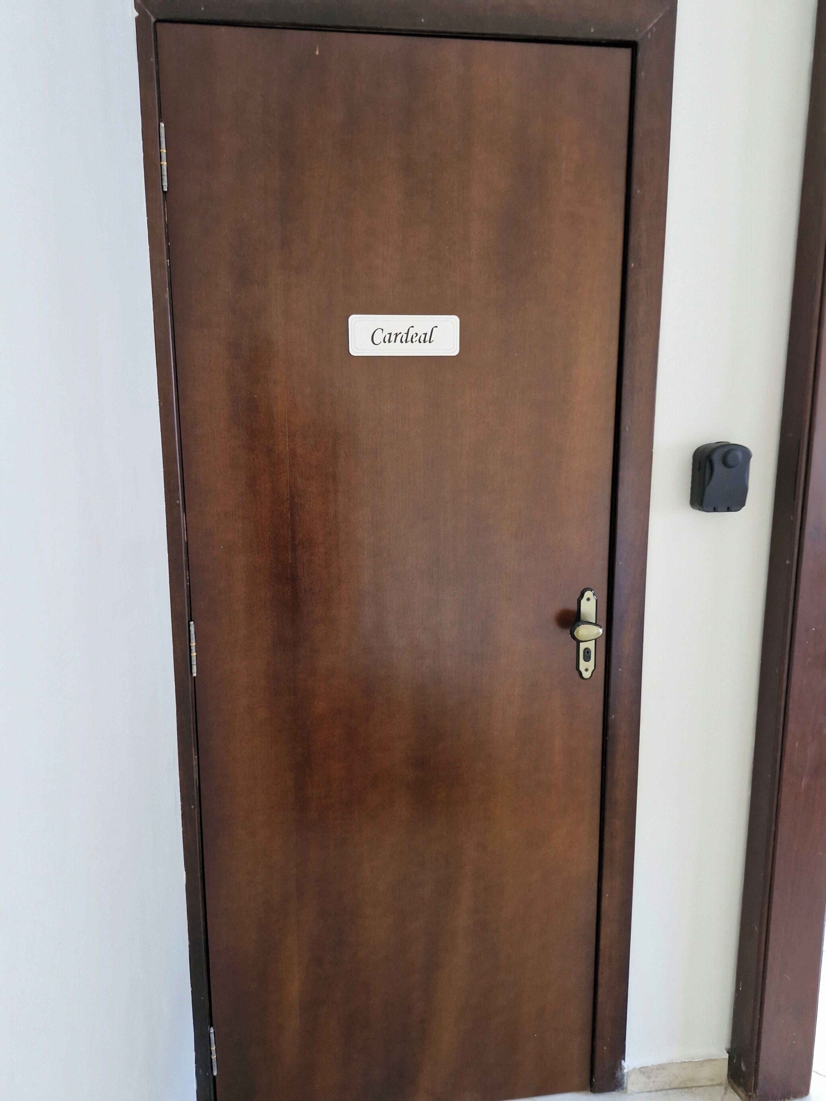 Una puerta de madera cerrada con una placa identificadora que dice 'Cardinal' y un picaporte.