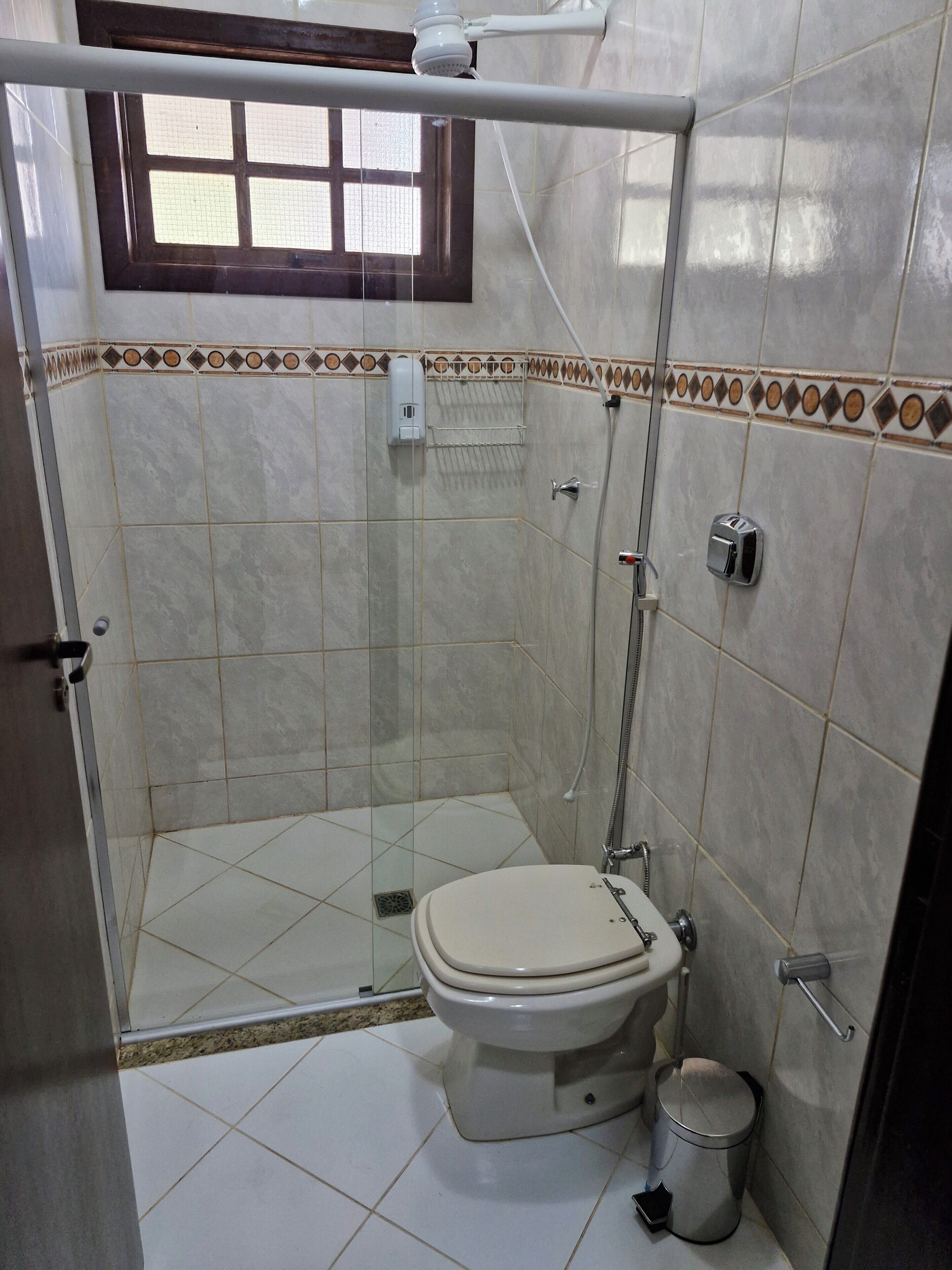 Casa de banho com chuveiro em cabine de vidro, sanita e um contentor de lixo.