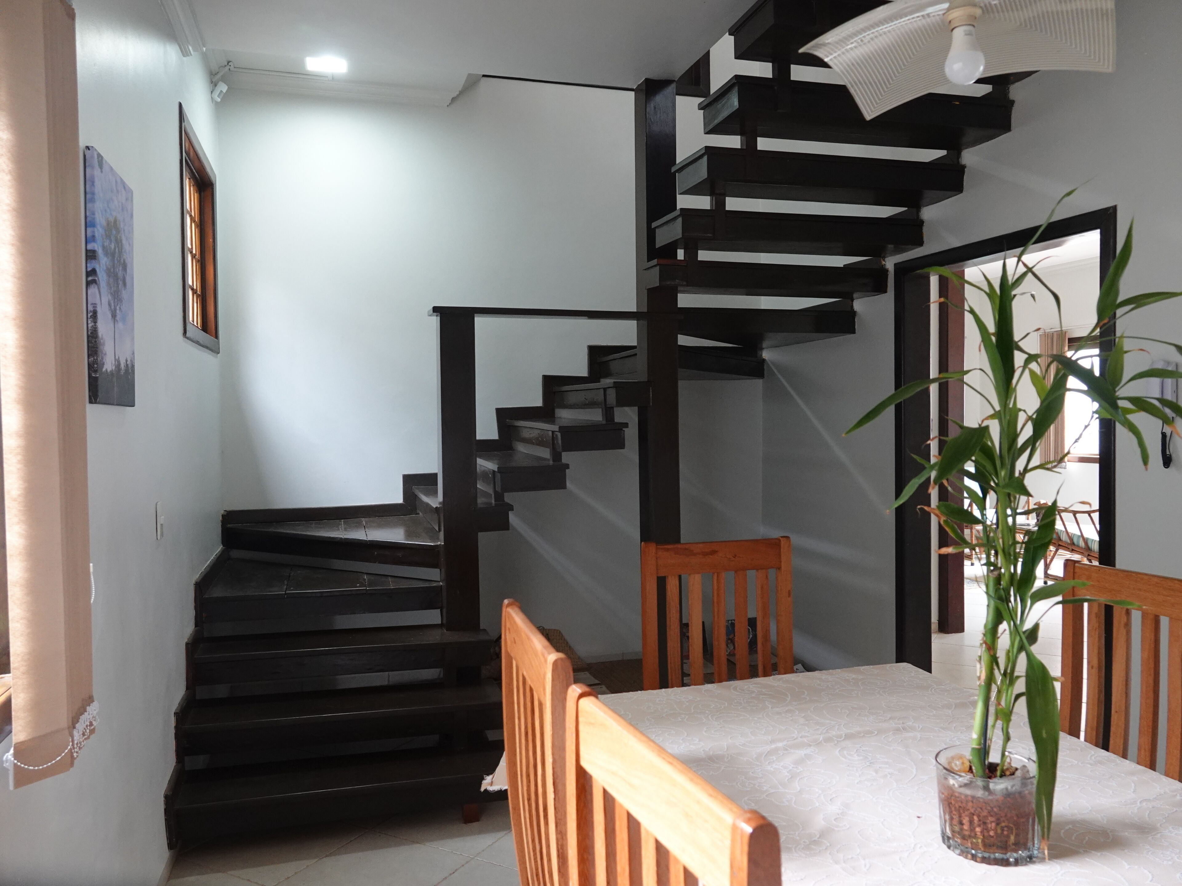 Uma escadaria com design moderno, uma mesa de jantar com cadeiras e um vaso de planta.