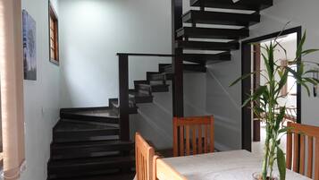 Uma escadaria com design moderno, uma mesa de jantar com cadeiras e um vaso de planta.