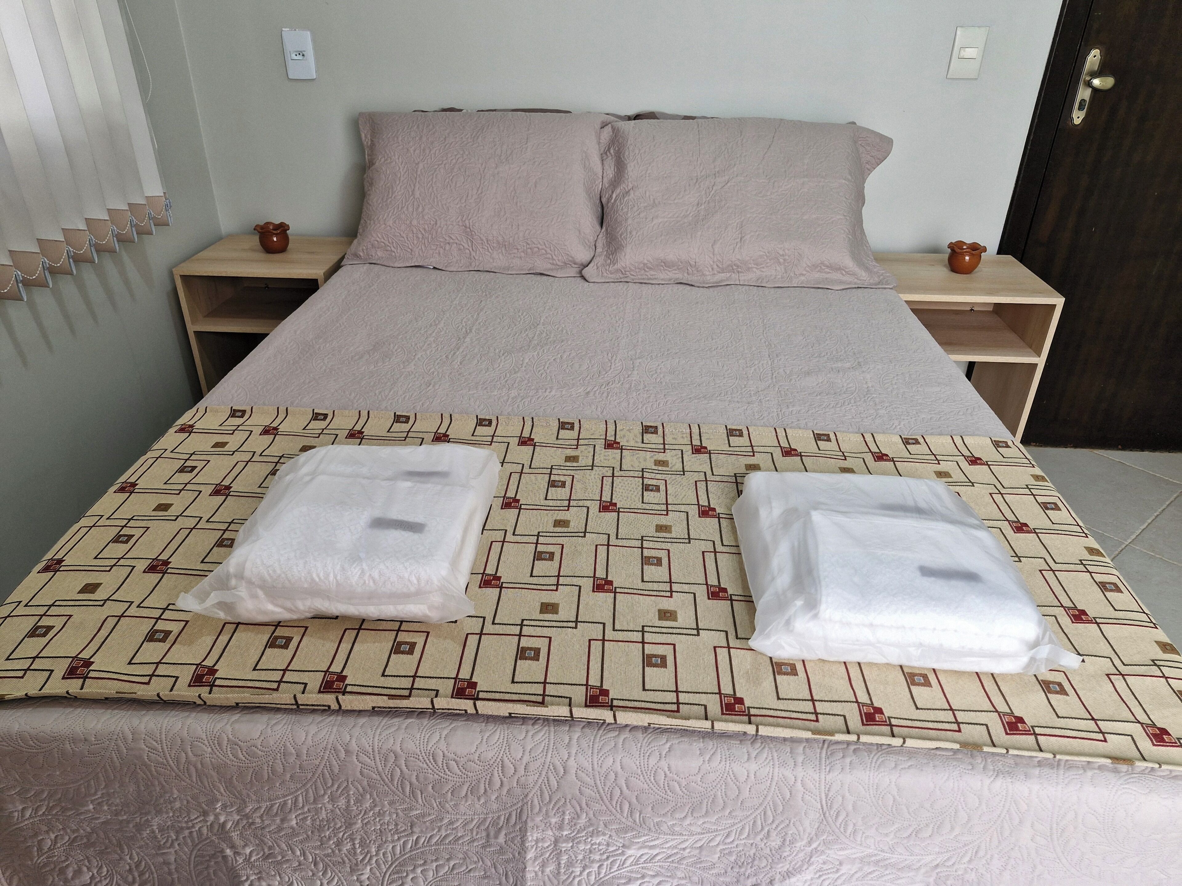 Una cama bien hecha con una colcha estampada, dos almohadas y dos toallas dobladas sobre la cama.