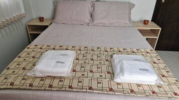 Una cama bien hecha con una colcha estampada, dos almohadas y dos toallas dobladas sobre la cama.