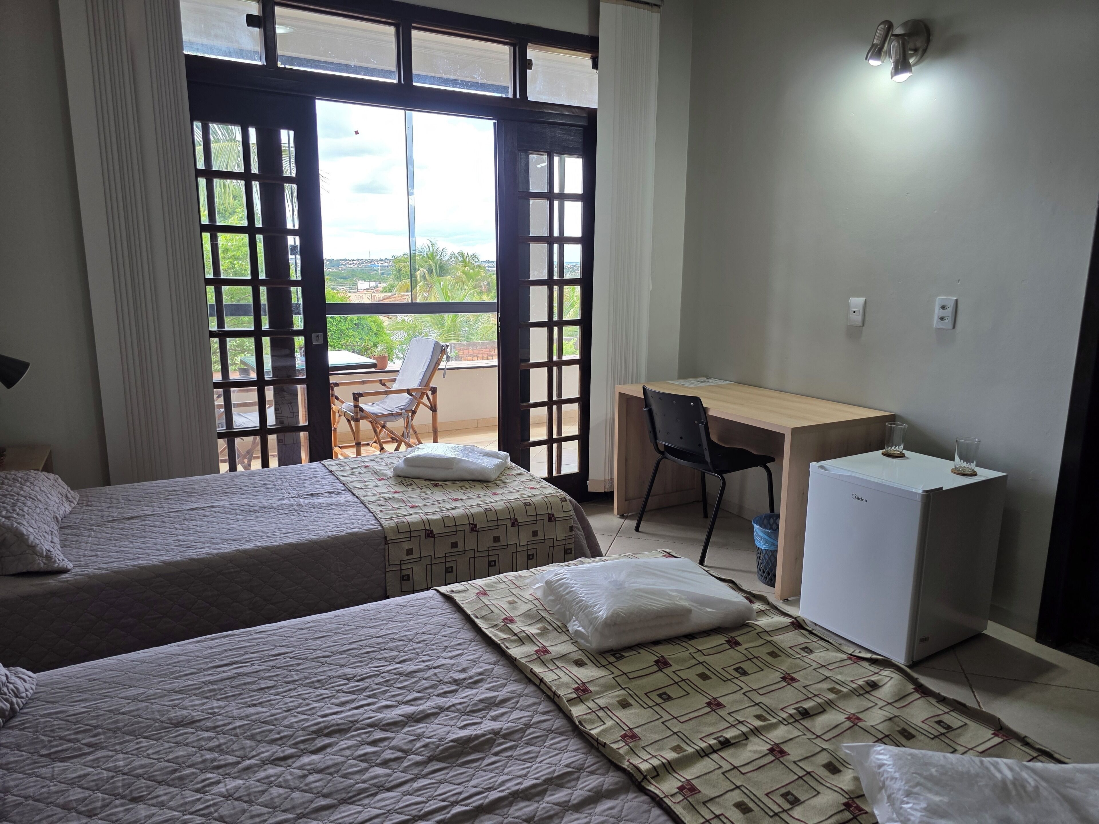 A hotel room with two beds, a desk, a chair, and a refrigerator.