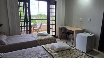A hotel room with two beds, a desk, a chair, and a refrigerator.