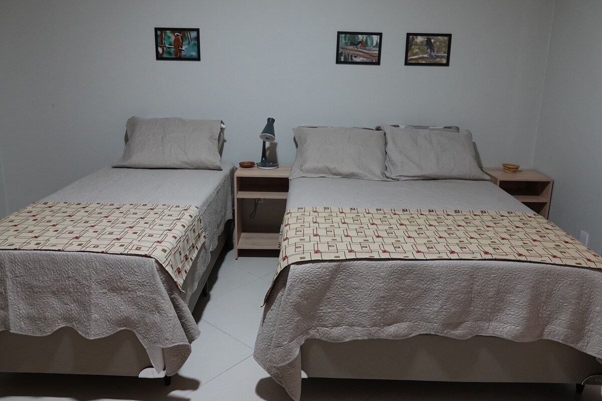 A bedroom with two single beds, each with a patterned bedspread and pillows, a bedside table with a lamp, and two framed pictures on the wall.