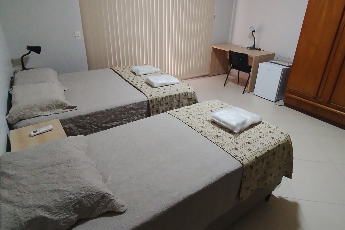 Een hotelkamer met twee bedden, een bureau, een stoel en een kleine koelkast.
