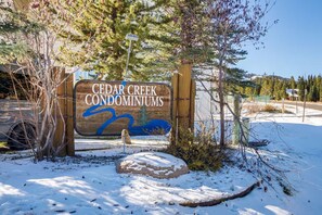 A wooden sign for Cedar Creek Condominiums with a blue river graphic. - Big Sky Condo - Ski/Ride in Shuttle Out (Big Sky)