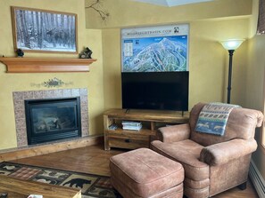 A living room with a fireplace, a television, a sofa, and a lamp. - Big Sky Condo - Ski/Ride in Shuttle Out (Big Sky)