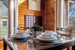 A wooden interior with a dining table set for four, featuring white plates, clear glassware, and a small potted plant. - Sleeps 6, Hot Tub, Arcade Loft, Kids Play Tent, 3.6 Mi to Dollywood (Sevierville)
